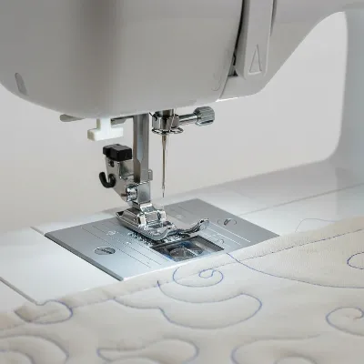 A close-up of a sewing machine's throat plate and feed dogs, highlighting LED lighting and a dropped feed dog mechanism for quilting. Fabric is underneath the needle, with quilting lines visible. Modern, well-lit studio setting, realistic.